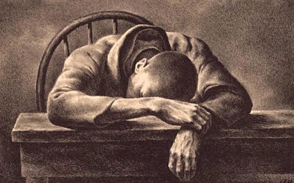 ID: a person of color in sepia tones leaning over a table as if lamenting.